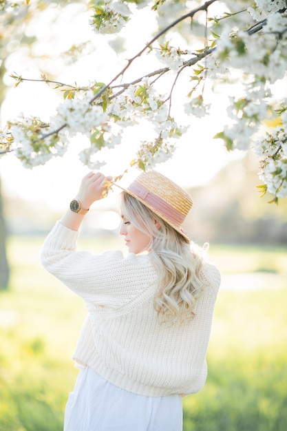Красивая молодая женщина в плетеной шляпе отдыхает на пикнике в цветущем саду