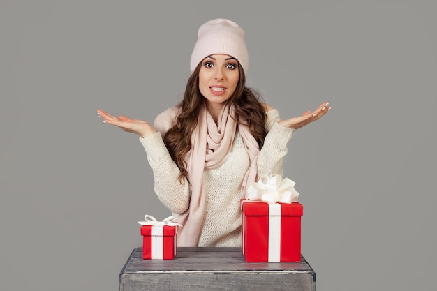 Красивая молодая женщина в зимней одежде задумчиво, нерешительно стоит перед выбором маленького или большого подарка на Новый год и Рождество. Какой подарок выбрать, решает девушка.