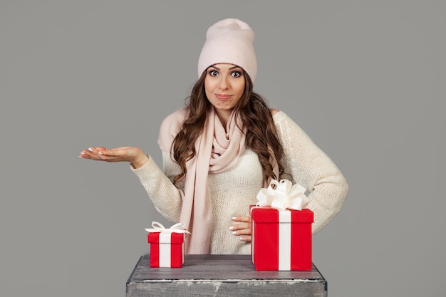 冬服を着た美しい若い女性は、思慮深く、ためらいながら、新年とクリスマスの小さな贈り物または大きな贈り物を選ぶ前に立っています。女の子はどの贈り物を選ぶかを決めます。