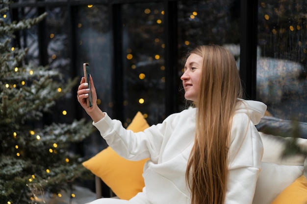 Bella giovane donna in tuta invernale cammina tra gli abeti e parla al telefono