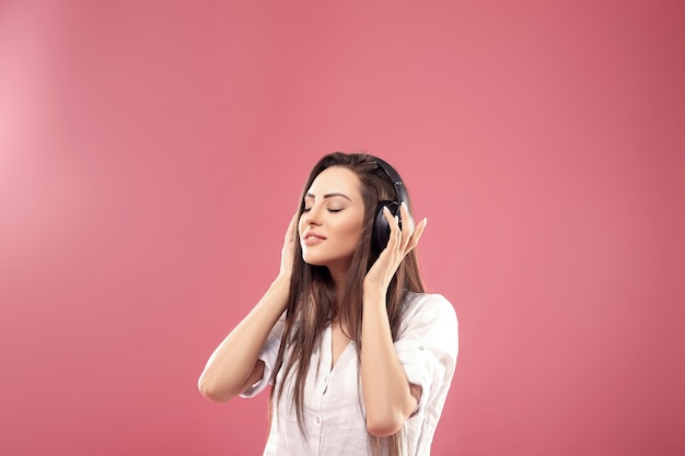 Beautiful young woman in wireless headphones listening to music using mobile