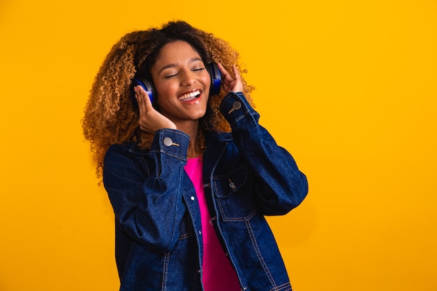 ヘッドフォンを笑顔で音楽を聴いているアフロ髪の美しい若い女性。