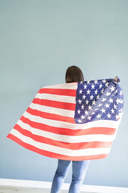 Красивая молодая женщина с американским флагом на синем фоне, вид сзади