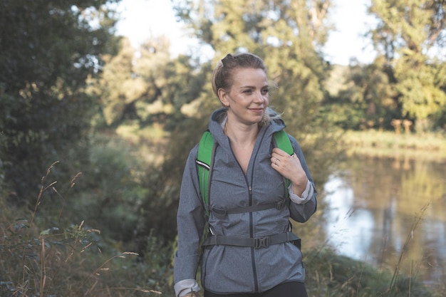 The beautiful young woman with a backpack is hiking in the forest