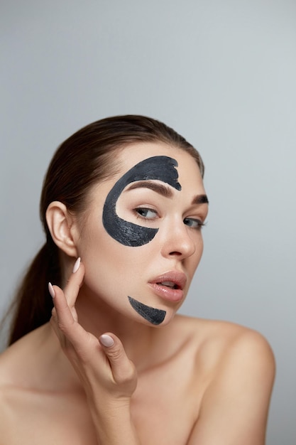 Beautiful Young Woman with Black Mask of Clay on fresh Face Facial treatment Cosmetology beauty