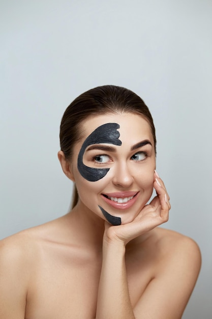 Beautiful young woman with black mask of clay on fresh face
facial treatment