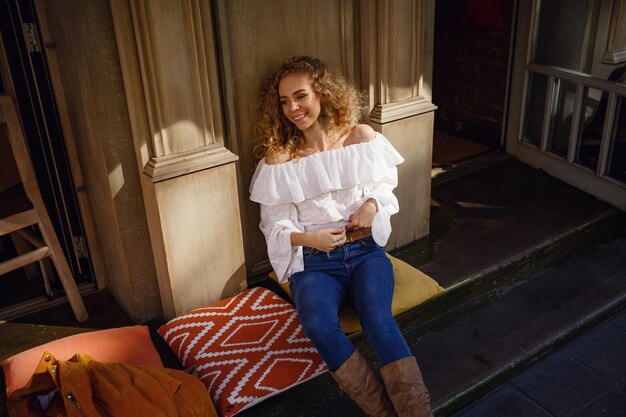 A beautiful young woman with blond curly hair walks through the sunny city, enjoys a lunch walk.