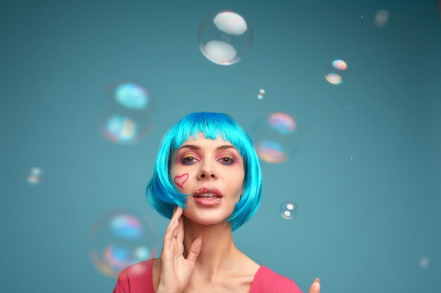 Beautiful young woman with blue wig and bright makeup in soap bubbles Fashion model girl with creative color makeup Women doll concept