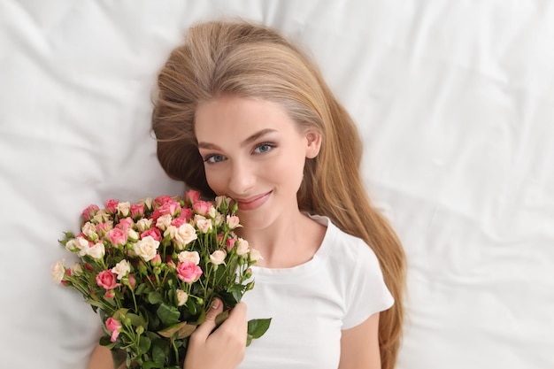 Beautiful young woman with bouquet of roses on bed at home