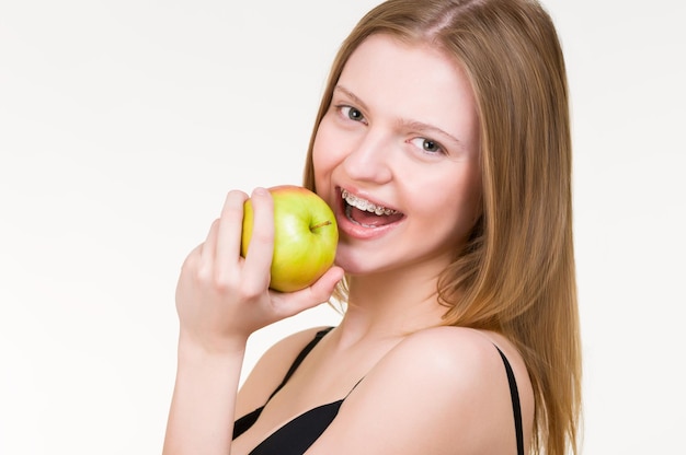 Beautiful young woman with brackets on teeth eating apple