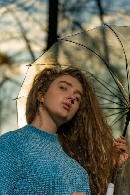 Красивая молодая женщина с каштановыми пышными непослушными волосами под прозрачным зонтиком за пределами Осеннего парка Вид снизу