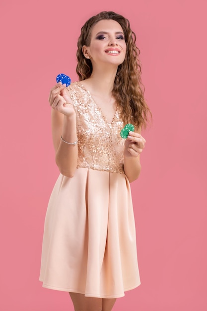 Beautiful young woman with casino chips on pink background