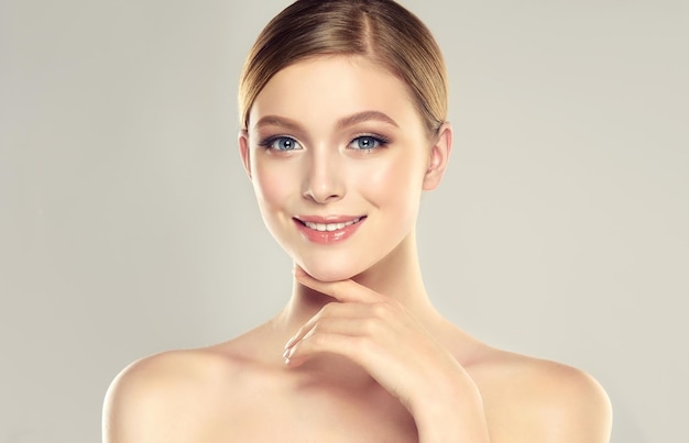 Beautiful young woman with clean fresh skin is touching own face Light smile on the perfect face