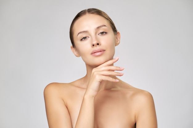 Beautiful young woman with clean fresh skin standing over light grey background