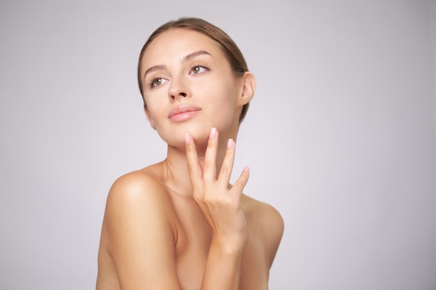 Beautiful young woman with clean fresh skin standing over light grey background