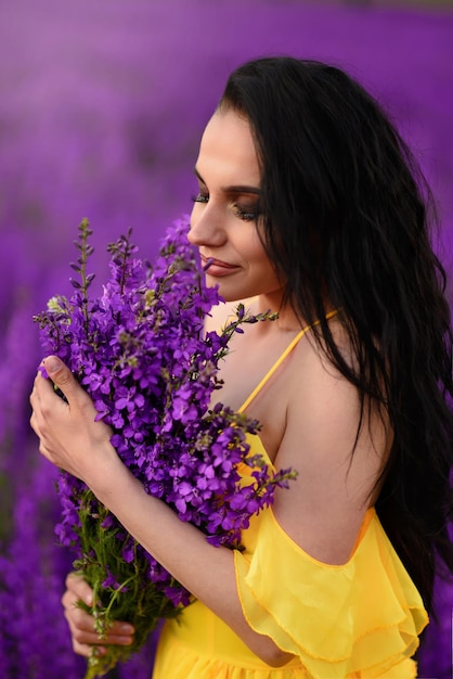 Foto bella giovane donna con gli occhi chiusi in un vestito giallo tiene in mano un mazzo di fiori viola. avvicinamento.