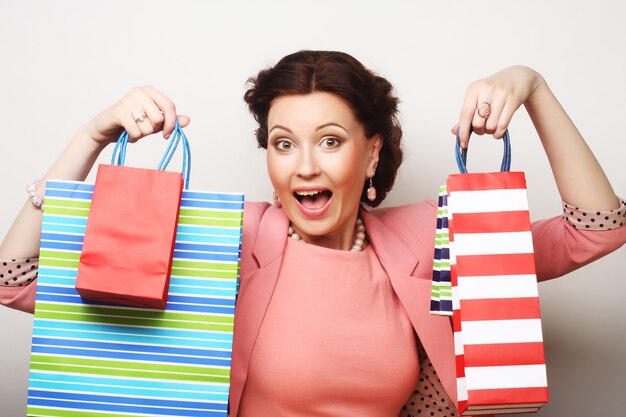 Beautiful young woman with colored shopping bags over grey background