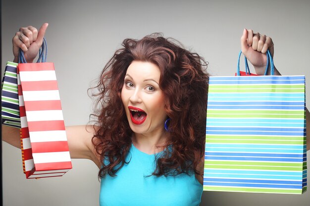 Beautiful young woman with colored shopping bags over grey background