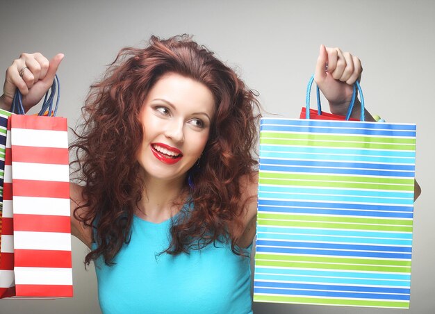 Beautiful young woman with colored shopping bags over grey background