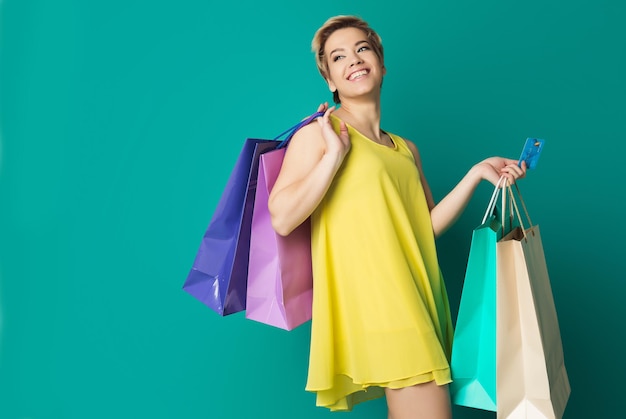 Beautiful young woman with colorful shopping bags over blue background, copy space