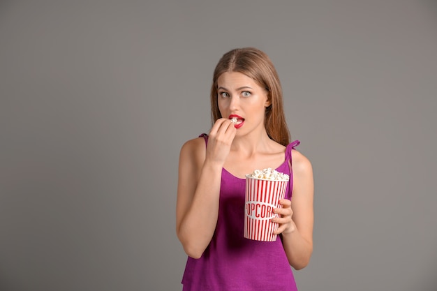 Beautiful young woman with cup of popcorn on grey surface