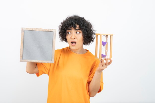 Photo beautiful young woman with curly hair holding frame with hourglass .