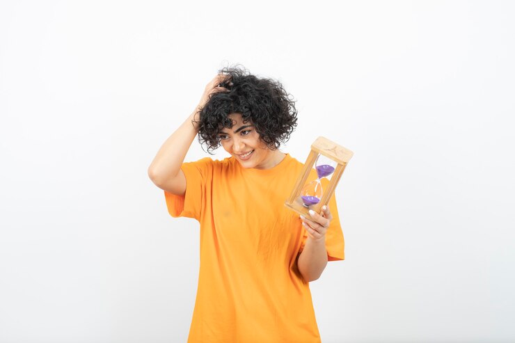 Beautiful young woman with curly hair holding hourglass .