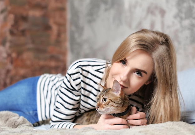 Beautiful young woman with cute cat on bed at home