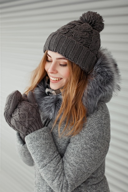 Beautiful young woman with a cute smile in a knitted hat and vintage gray mittens