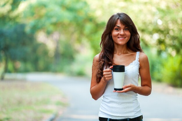 Bella giovane donna con una tazza di caffè usa e getta, bevendo caffè nelle sue mani