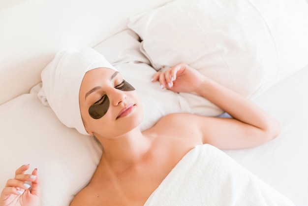 Beautiful young woman with under eye patches in bathrobe lying in bed Happy girl taking care of herself Beauty skincare and wellness morning concept