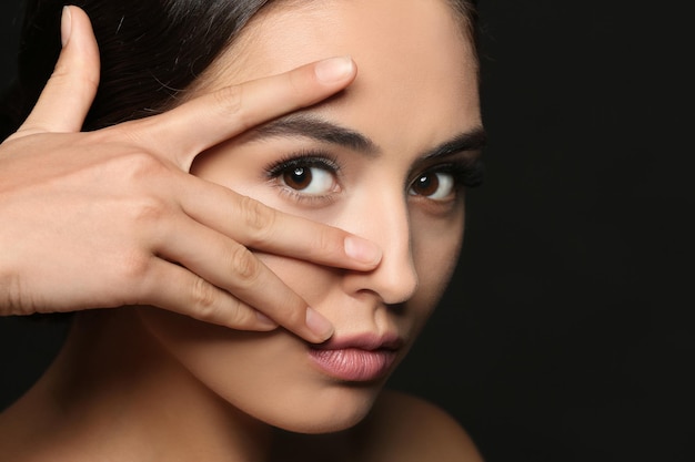 Beautiful young woman with eyelash extensions on dark background