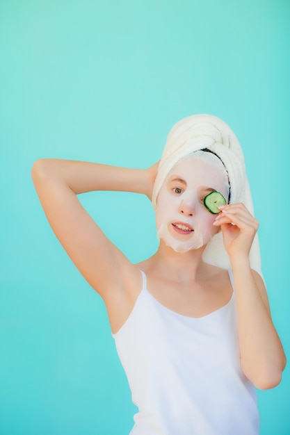 Beautiful young woman with facial mask on her face holding slices of cucumber.