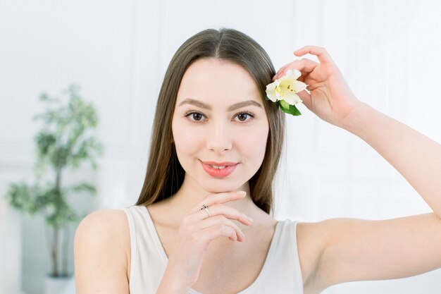 Beautiful young woman with flower in hand near at face. Closeup portrait of caucasian girl with healthy clean skin.