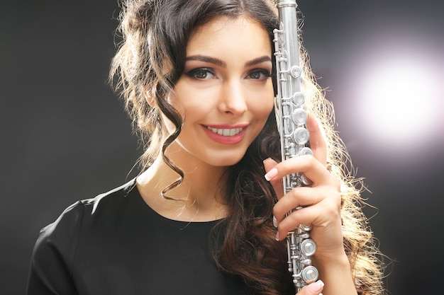 Beautiful young woman with flute on dark surface