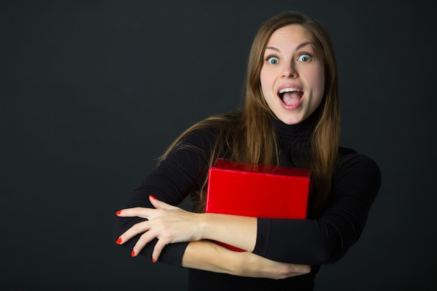 Beautiful young woman with a gift in hand on a black background