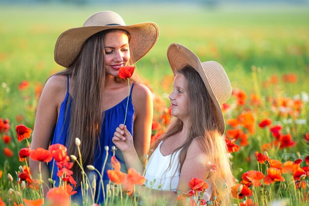 Bella giovane donna con la ragazza in cappelli di paglia nel campo di papaveri famiglia felice divertendosi in natura