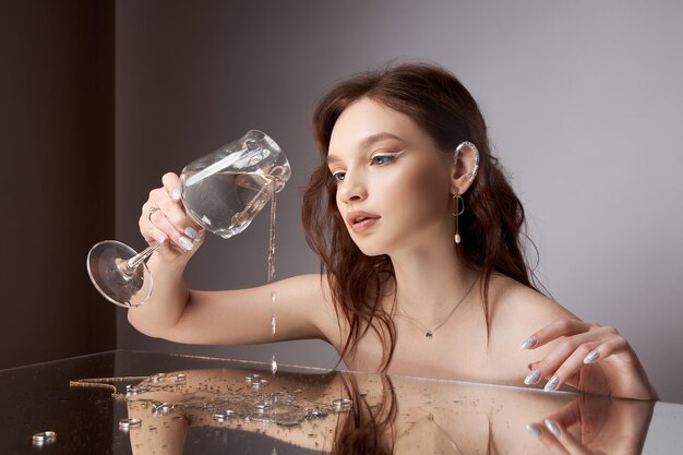 Beautiful young woman with a glass and jewelry in her hands