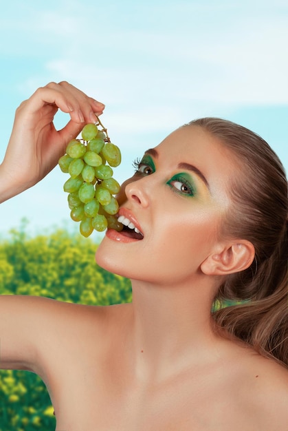 Beautiful young woman with grape bunches on summer green and yellow background