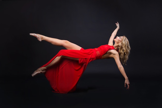 beautiful young woman with hairstyle and make-up in a red dress in flight on a black background