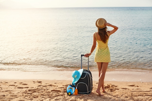 Beautiful young woman with a hat standing with suitcase on the wonderful sea