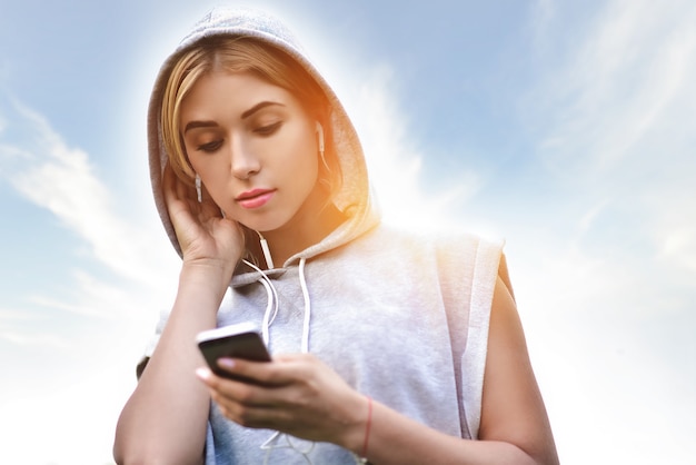 Beautiful young woman with headphones glad after nice jogging in city park