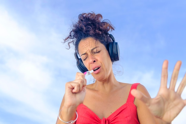 Photo beautiful young woman with headphones listening to music and dancing with the sky in the background