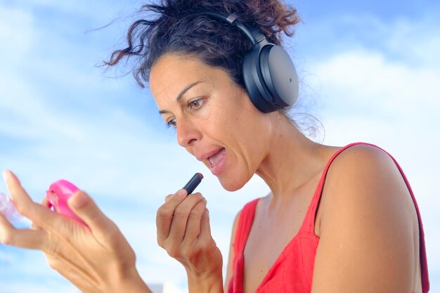 Beautiful young woman with headphones listening to music and painting her lipstick on