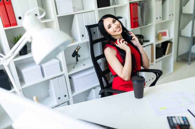 Beautiful young woman with headphones on neck sitting in office at table.