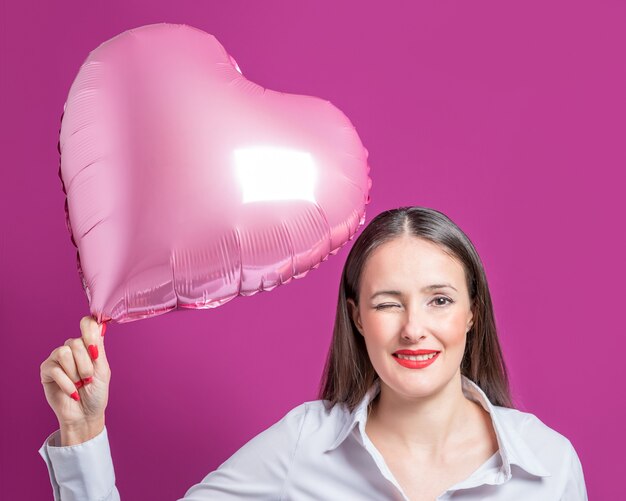 Foto bella giovane donna con un palloncino a forma di cuore su uno sfondo luminoso