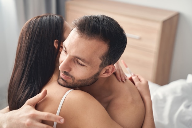 Beautiful young woman with her eyes closed embracing her dark-haired Caucasian husband in a bedroom