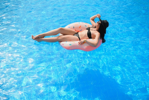 Beautiful young woman with inflatable donut in blue swimming pool