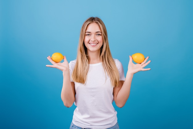 Beautiful young woman with lemons in hands on blue