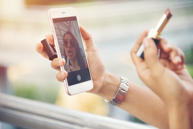 Beautiful young woman with lipstick looking at smartphone.